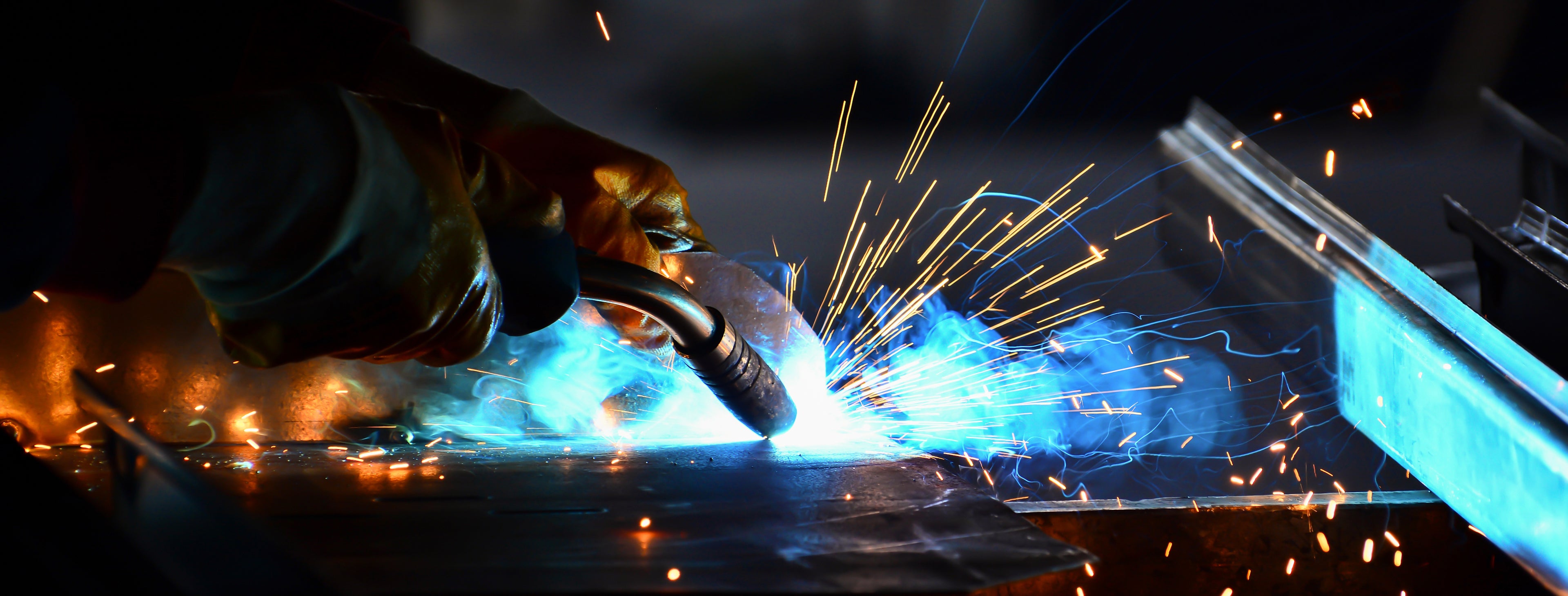 Person welding metal with sparks flying, wearing protective gloves.