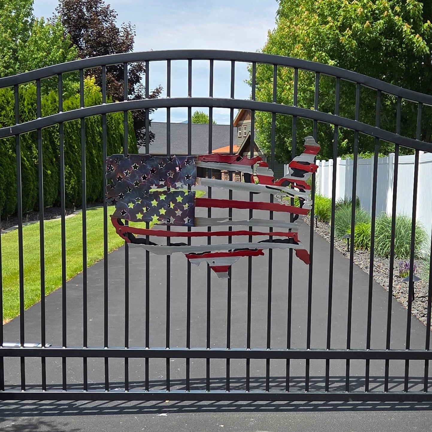 Metal American Flag on Black metal gate on a driveway with a house and trees in the background